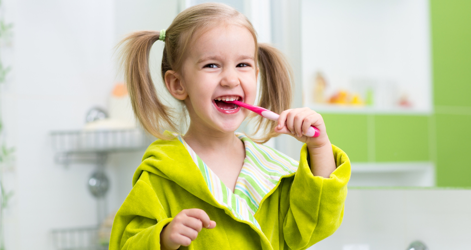 Smiling child kid girl brushing teeth in bathroom